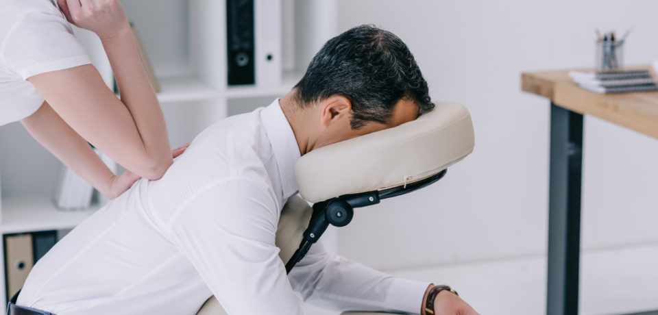 professional masseuse doing seated back massage for businessman at office